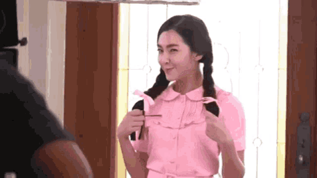 a woman in a pink dress is standing in front of a door holding a comb in her hand .