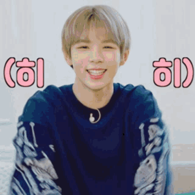 a young man wearing a blue sweater is smiling in front of a wall with chinese writing on it .