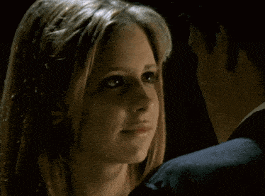 a close up of a woman 's face with a man in a suit behind her