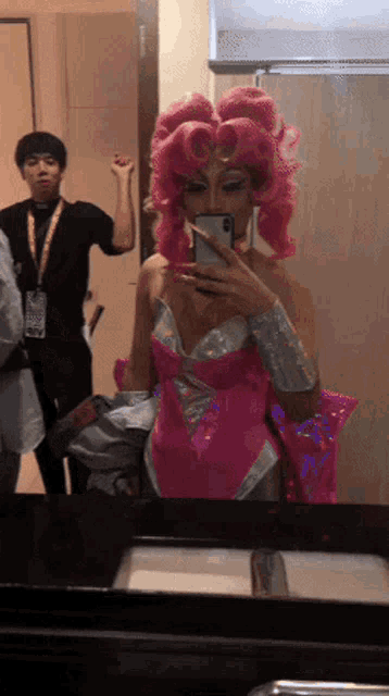 a woman in a pink wig is taking a picture of herself in a mirror