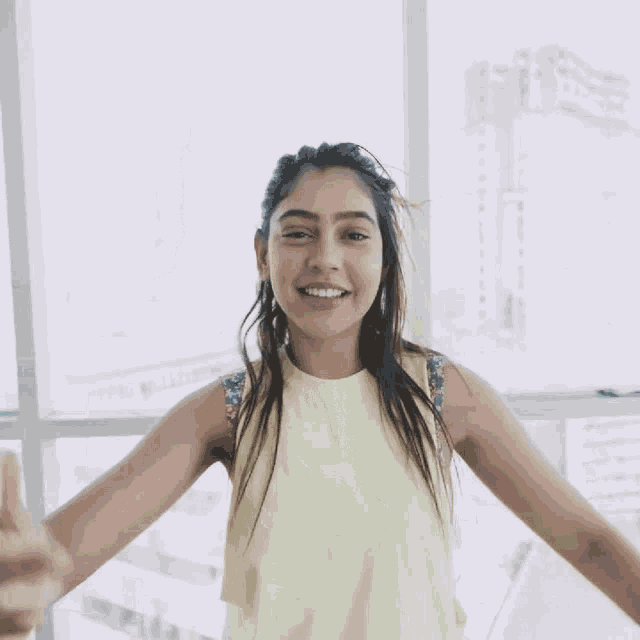 a young woman in a yellow tank top stands in front of a window