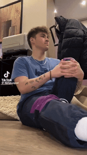 a man in a blue shirt is sitting on the floor with his legs crossed and a tiktok watermark on the bottom