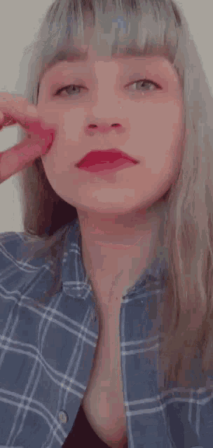 the woman is wearing a plaid shirt and red lipstick and is covering her ears with her hand .