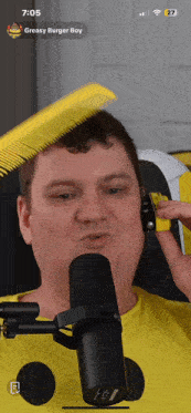 a man combs his hair in front of a microphone and a screen says greasy burger boy