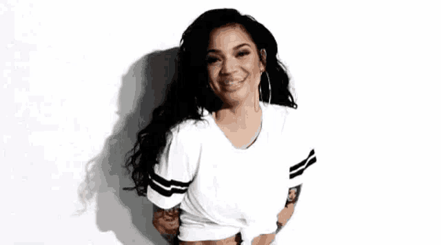 a woman wearing a white t-shirt and hoop earrings is standing in front of a white wall .