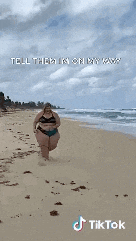 a woman in a bikini is walking on the beach and says `` tell them im on my way '' .