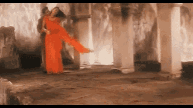 a woman in an orange dress is dancing with a man in a room with columns