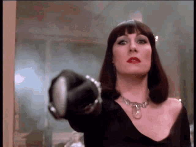 a woman in a black dress and necklace is pointing at something .