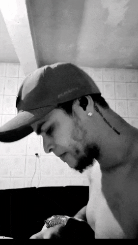 a man without a shirt is wearing a baseball cap and has a tattoo on his neck