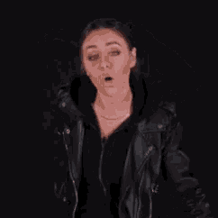 a woman wearing a black leather jacket is making a funny face .