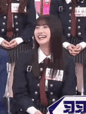 a woman in a suit and tie is laughing while sitting in front of a group of girls .