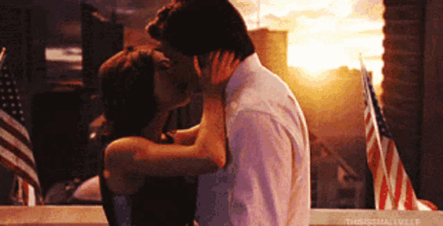 a man and a woman are kissing in front of an american flag