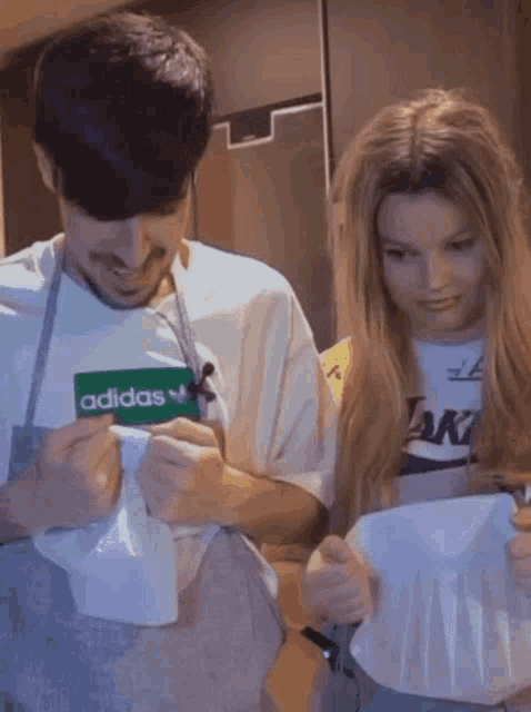 a man and a woman wearing aprons are looking at a card that says adidas