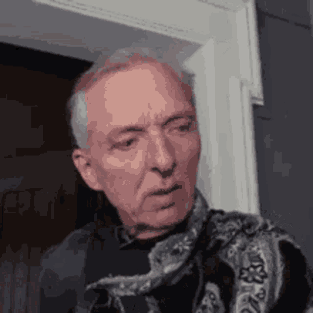 a man with gray hair and a scarf around his neck is standing in front of a door .