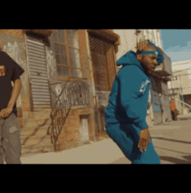 a man in a blue hoodie is dancing on a street