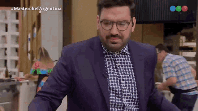 a man in a suit and polka dot shirt is standing in front of a screen that says masterchef argentina