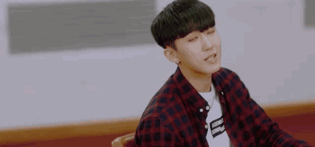 a young man in a plaid shirt is sitting in a chair and making a funny face .