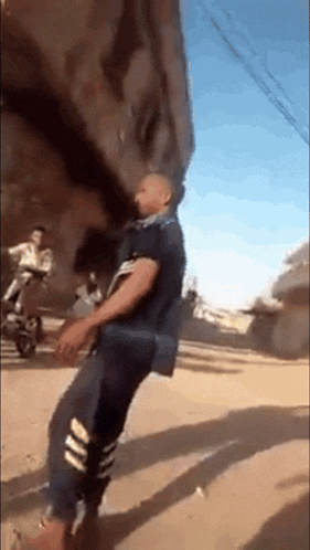 a man in a black shirt and striped pants is standing on a dirt road