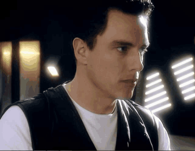 a close up of a man 's face with a white shirt and a black vest