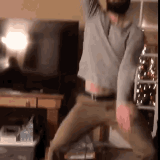 a man with a beard is dancing in a living room with a christmas tree in the background