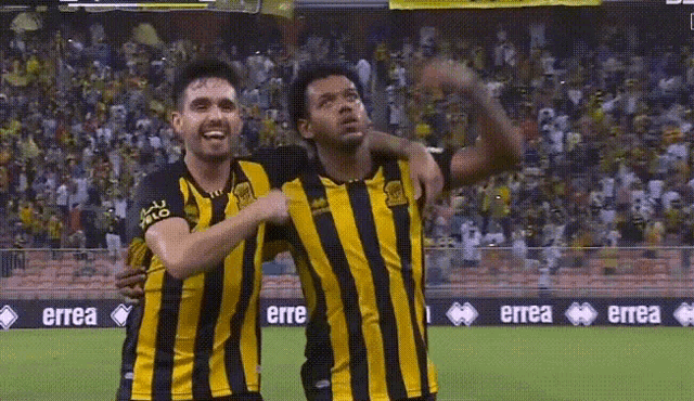 two soccer players are hugging on a field with a banner for errea in the background