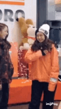 a woman in an orange jacket is standing next to a stuffed animal