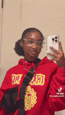 a woman in a red hoodie is taking a selfie in a mirror .