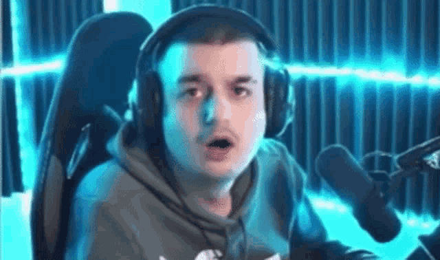 a man wearing headphones and a hoodie is sitting in front of a microphone and making a funny face .