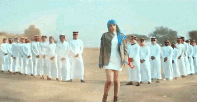 a woman in a blue turban is standing in front of a group of men in white clothes .
