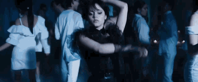 a woman in a black dress is dancing in front of a crowd of people in a dark room .
