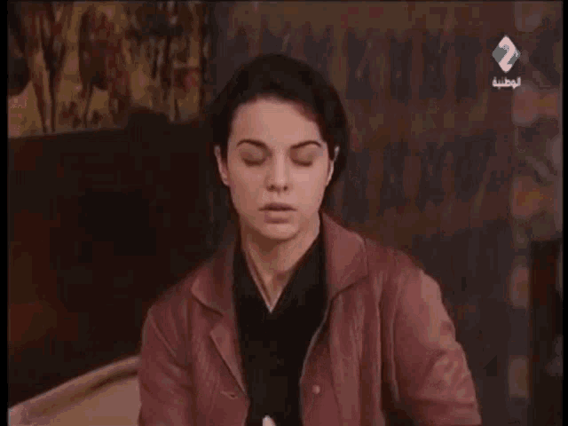 two women are sitting on a bed talking to each other and one of them is holding her chest .