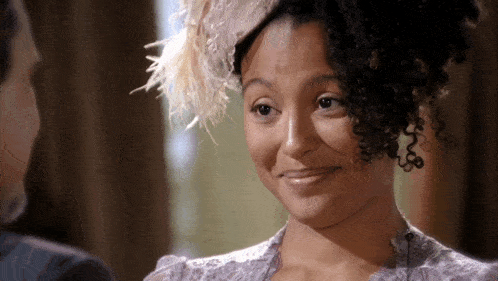 a woman with curly hair wearing a feathered hat is smiling