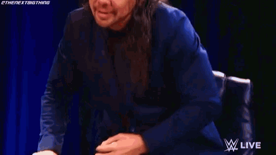 a man with long hair is laughing and saying `` last man standing '' while wearing a blue shirt .