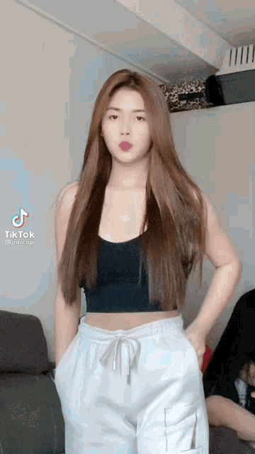 a woman wearing a black crop top and white sweatpants is standing in a living room .