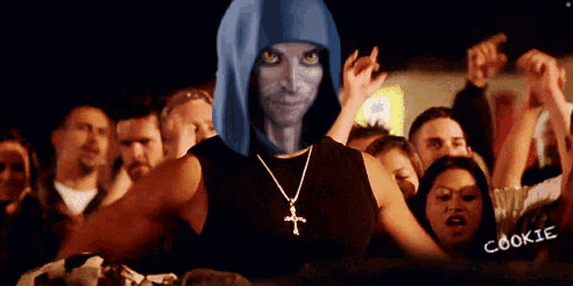 a man wearing a blue hood and a cross necklace stands in front of a crowd with the word cookie on the bottom right