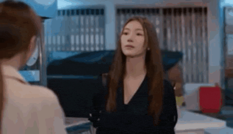 a woman with long hair is standing next to another woman in a room and looking at the camera .