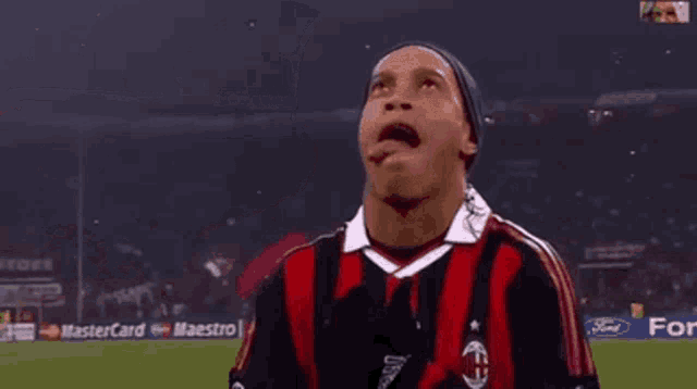 a soccer player wearing a black and red adidas jersey is making a funny face .
