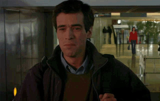 a man wearing a brown sweater and a black jacket is standing in a hallway