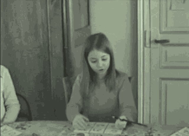 a young girl is sitting at a table with a pen in her hand .
