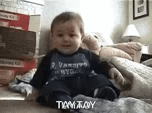 a baby wearing a varsity byg shirt is sitting on the floor .