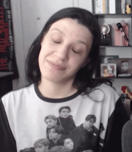 a woman wearing a t-shirt with a picture of a group of people on it is making a funny face .