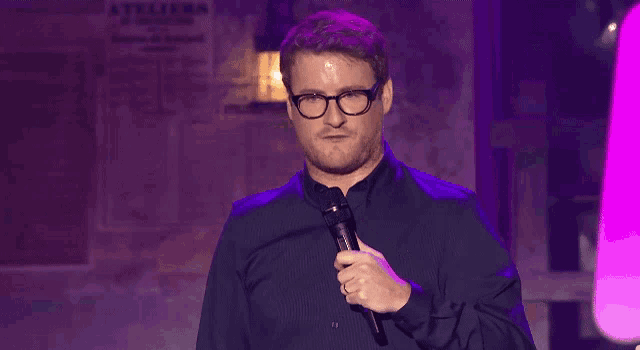 a man wearing glasses and a black shirt is holding a microphone and making a funny face