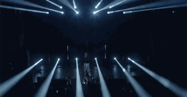 a woman is standing in front of a crowd on a stage with a lot of lights