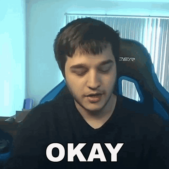 a man in a black shirt is sitting in a gaming chair and says okay