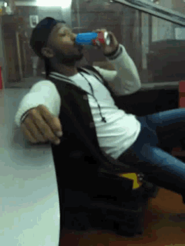 a man is drinking from a blue can while sitting on a chair