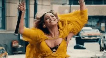 a woman in a yellow dress is standing on a street with her arms in the air and smiling .