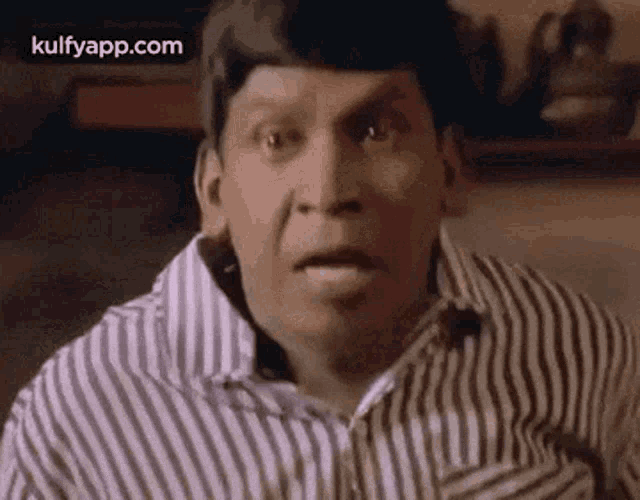 a man in a striped shirt is making a funny face and looking at the camera .