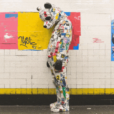 a person in a bear costume is standing in front of a wall with graffiti on it that says ' zest ' on it