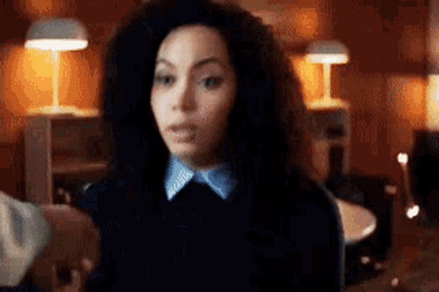 a woman with curly hair and a blue collar is standing in a room with lamps .