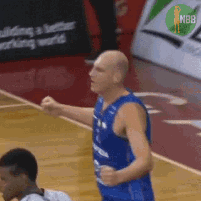 a bald man in a blue basketball jersey stands on a court
